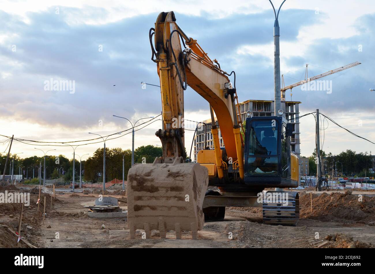 Escavatore in cantiere. Il retroescavatore scavare il terreno per la fondazione, mettendo in posa tubi fognari. Installazione di impianti idrici principali. Hea Foto Stock