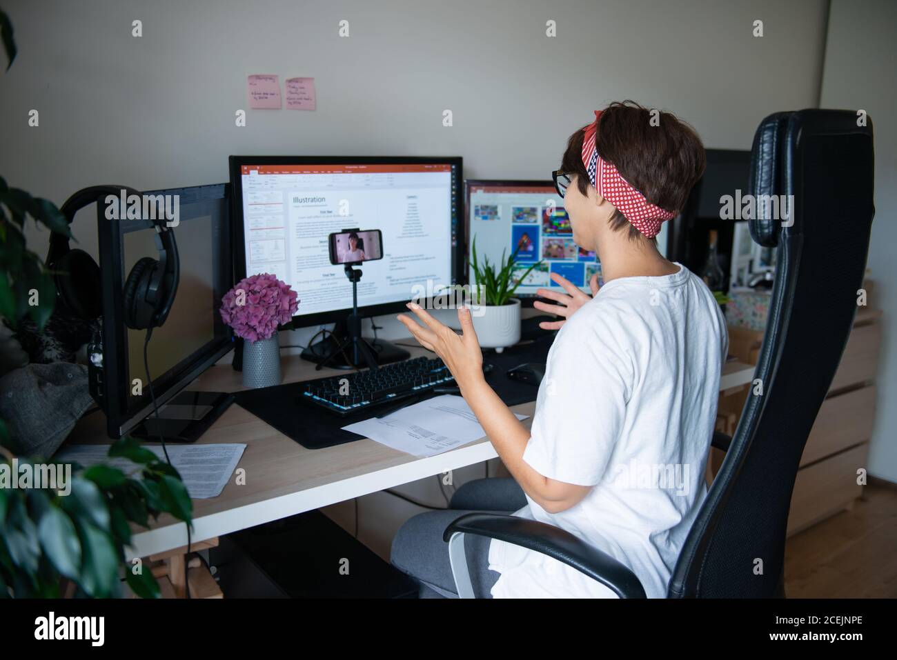 Indietro guardare creativo blogger ripresa video sulla fotocamera del telefono seduto alla sua scrivania con pochi monitor a casa spazio di lavoro. E-learning. Lavoro remoto Foto Stock