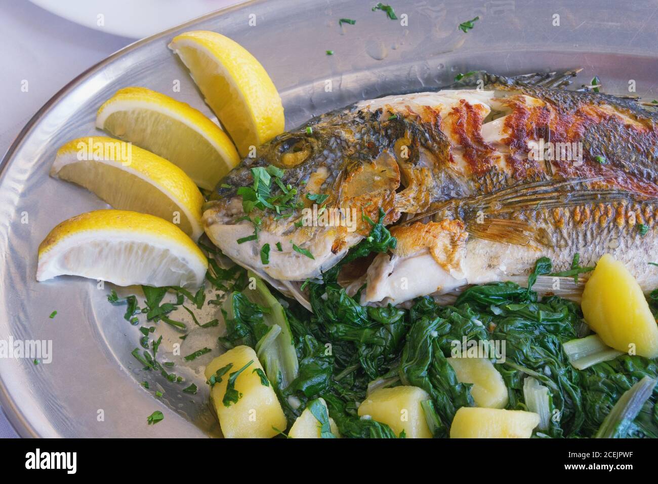 Cucina balcanica. Pesce alla griglia (orata di mare) con verdure a foglia verde e fette di limone Foto Stock