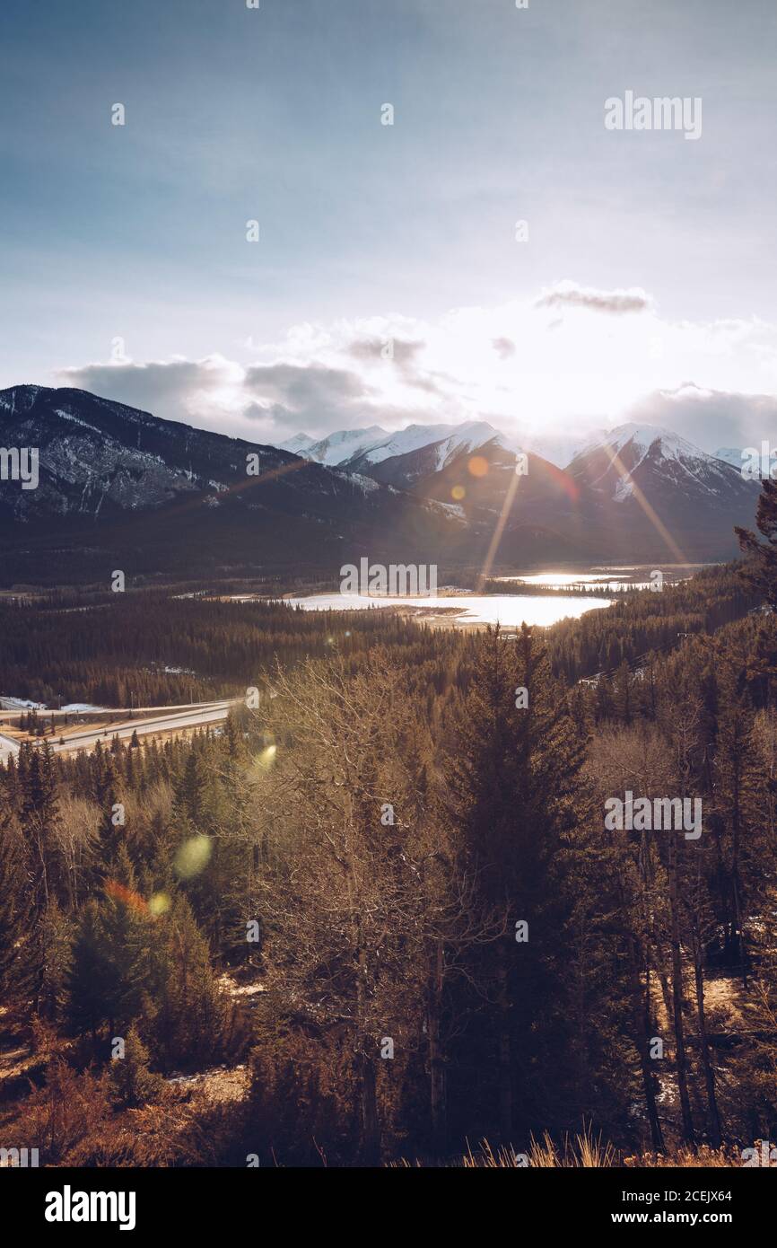 Sole luminoso che splende sul cielo con poche nuvole su autunnale Foresta canadese sullo sfondo con montagne innevate e piccolo lago Foto Stock