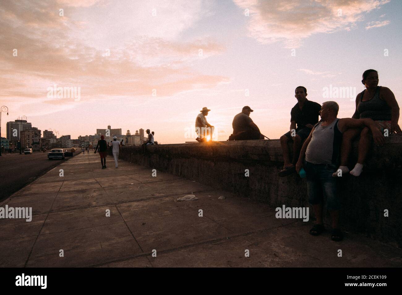 Abitanti cubani che si agghiacciano sul lungomare pedonale di cemento sullo sfondo del cielo del tramonto, Foto Stock