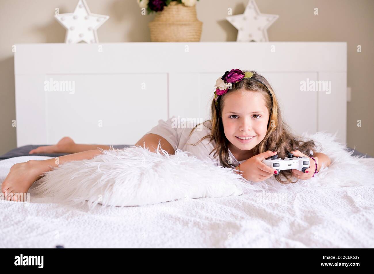 Una bambina sta giocando una console per computer su un divano in una stanza luminosa. Giochi simultanei per bambini. Joystick per il controllo manuale. Emozioni e divertimento del bambino. Spazio di copia. Alta qualità. Messa a fuoco morbida Foto Stock
