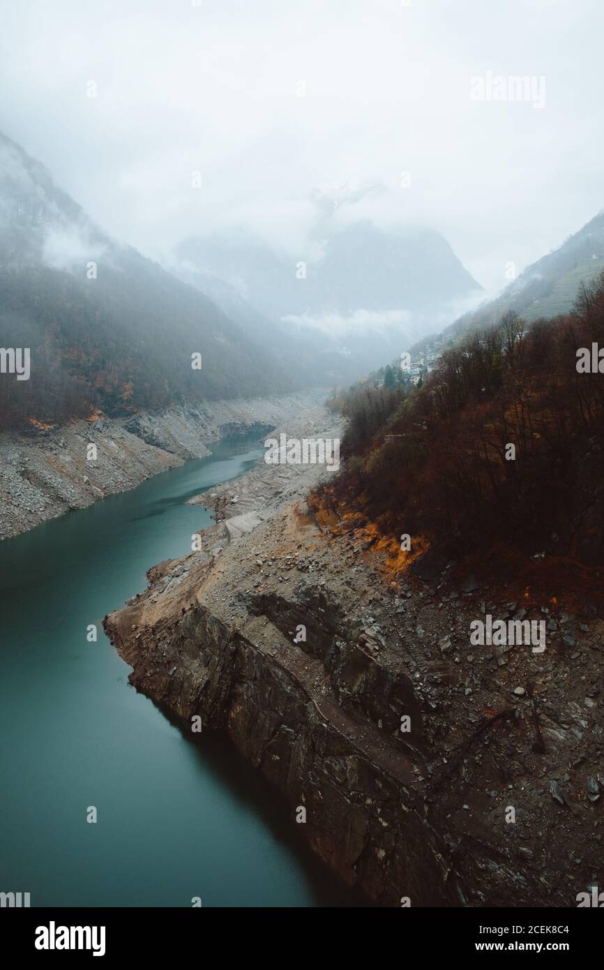 Piccolo fiume blu che scorre tra due colline in autunno nebbia giorno. Foto Stock