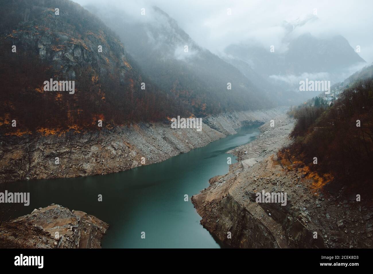 Piccolo fiume blu che scorre tra due colline in autunno nebbia giorno. Foto Stock