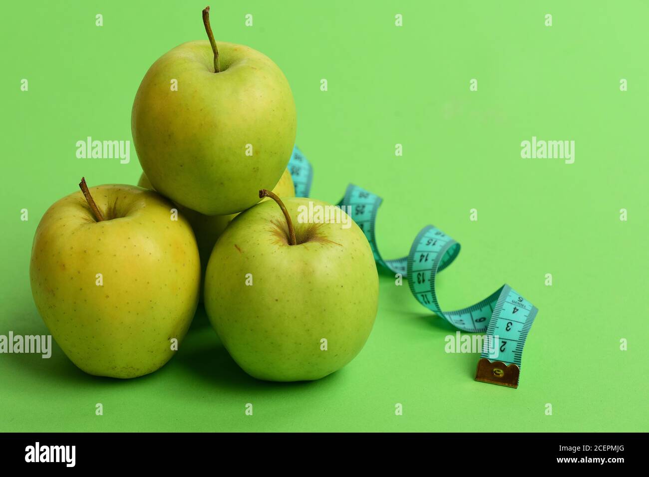 Simboli sportivi e di regime sano. Concetto di regime di dieta e sport. Mele di colore verde brillante e nastro di misurazione ritorto su sfondo verde. Metro a nastro in colore ciano vicino a frutta succosa, primo piano Foto Stock