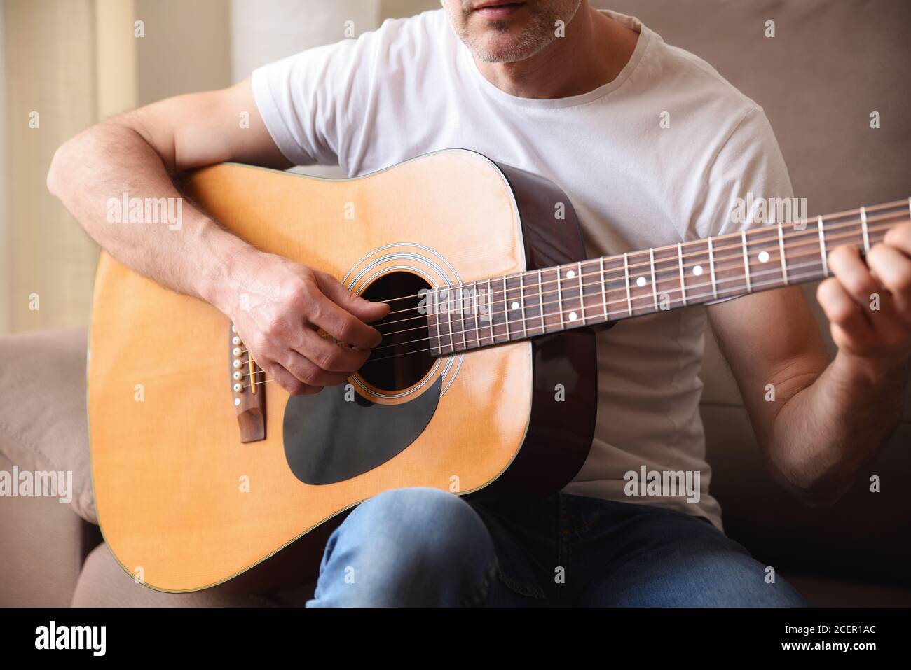 Dettaglio del corpo della chitarra acustica e dell'uomo che suona con il bianco camicia a manica corta e jeans blu Foto Stock