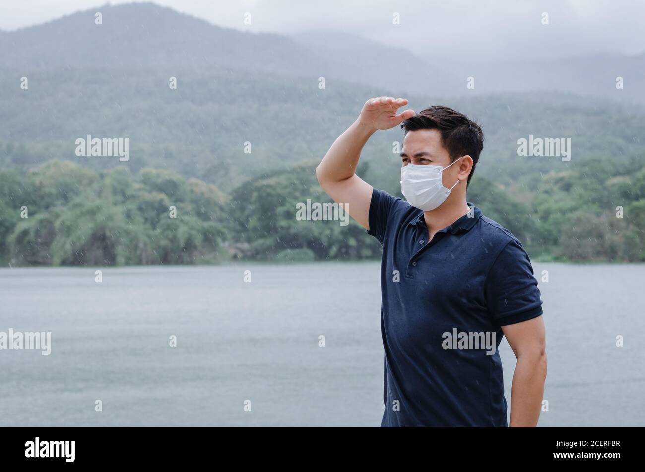 Uomo asiatico indossare maschera viso per proteggere dal virus e bagnarsi dalla pioggia nella stagione monsonica. Foto Stock