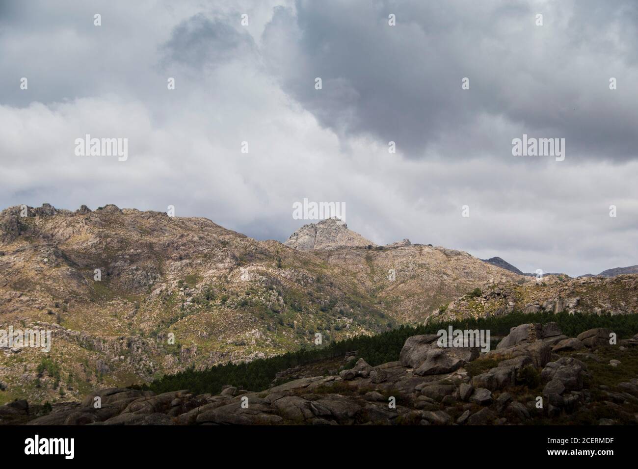 Vetta di montagna che mostra in lontananza, dietro più montagne e valli, ombreggiate da un cielo nuvoloso Foto Stock