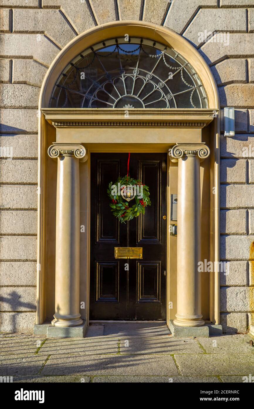Porta d'ingresso georgiana, decorata per Natale con corona verde e bacche rosse. Dublino, Irlanda. Ingresso con colonne in pietra e fanale Foto Stock