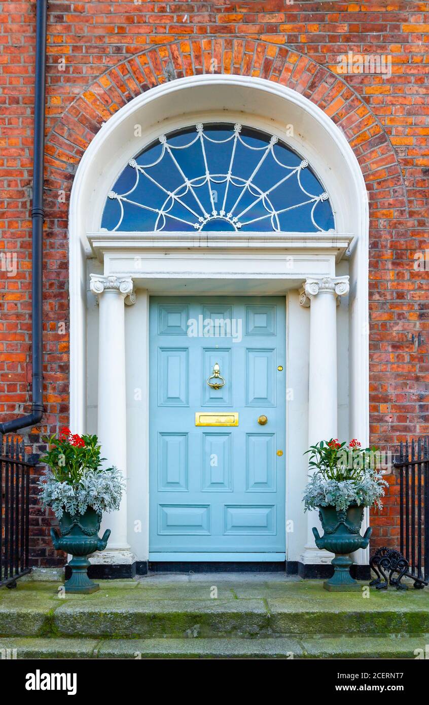 Porta d'ingresso in stile georgiano, dipinta di blu, con fanale decorativo ad arco, colonne in pietra e pentole di piante. Raschietto in ferro, ringhiere. Dublino, Irlanda Foto Stock