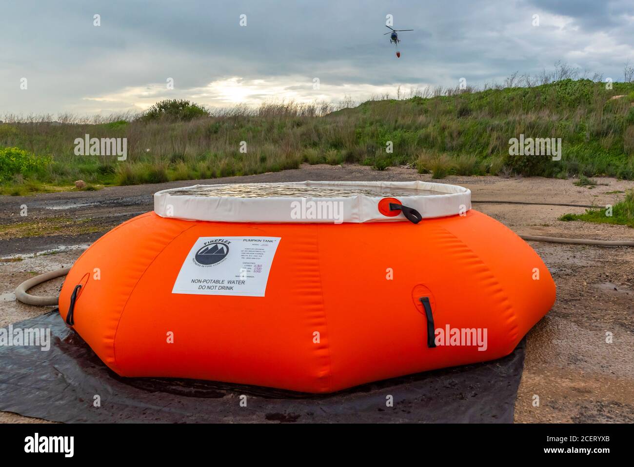 Un elicottero di polizia viene utilizzato durante un'esercitazione antincendio per sollevare l'acqua verso la zona di fuoco. Il contenitore dell'acqua viene riempito da un serbatoio di zucca gonfiabile Foto Stock