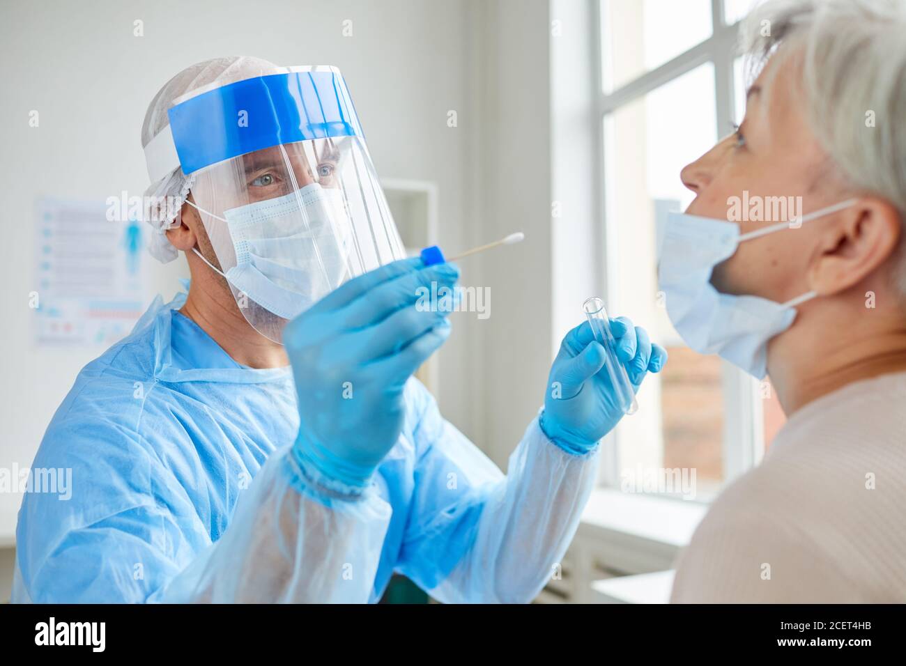 Lavoratore medico professionista che indossa dispositivi di protezione personale che testano la donna anziana per malattie pericolose utilizzando il bastone di prova Foto Stock