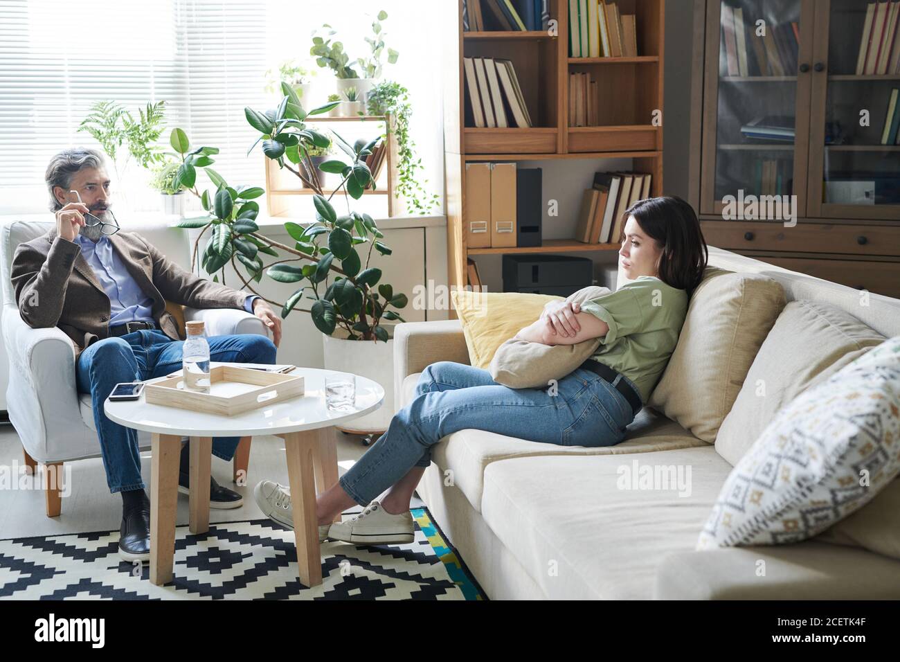 Giovane donna malinconica seduta sul divano abbracciando cuscino che la condivide pensieri allo psicologo durante la sessione di terapia Foto Stock