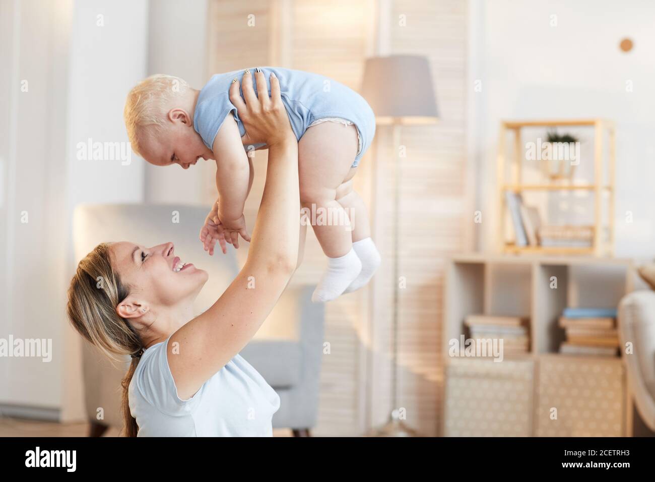 Vista laterale orizzontale di una giovane madre felice che tiene il suo bambino bambino sopra la testa, copia spazio Foto Stock