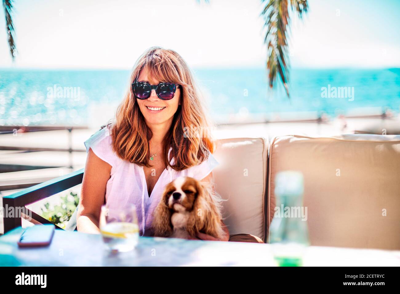 Foto di donna di mezza età godendo di una giornata di sole mentre si rilassa sul mare con il suo cucciolo di cavalier re charles. Foto Stock