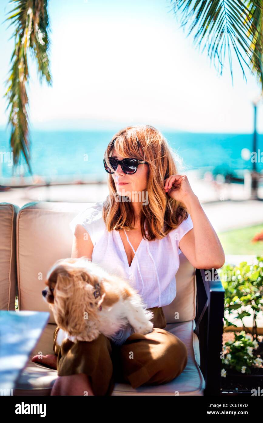 Foto di donna di mezza età godendo di una giornata di sole mentre si rilassa sul mare con il suo cucciolo di cavalier re charles. Foto Stock
