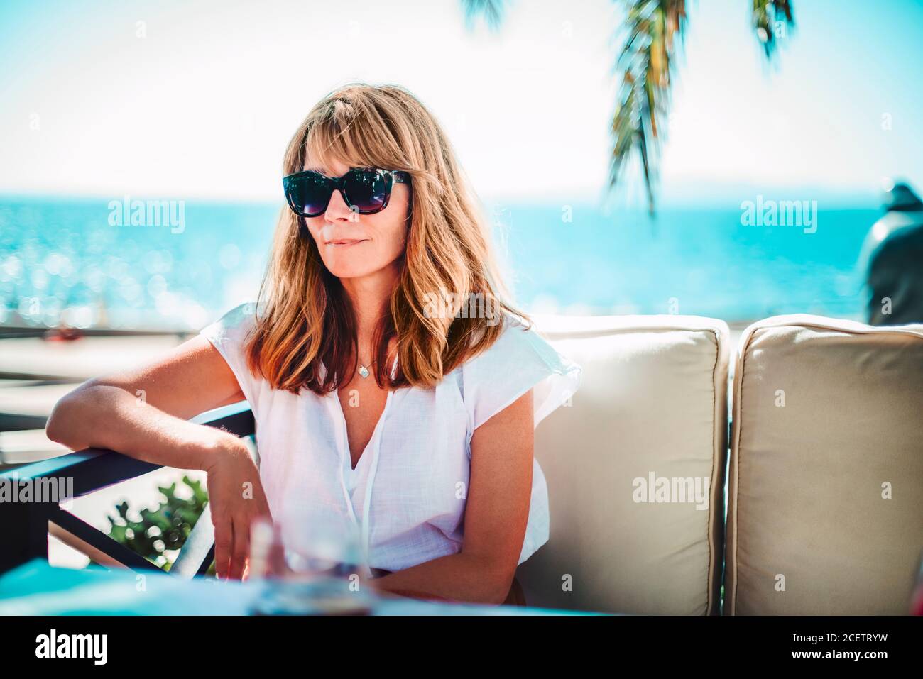 Ritratto di una donna felice che gode del sole estivo mentre si rilassa sul divano lounge vicino al mare. Foto Stock