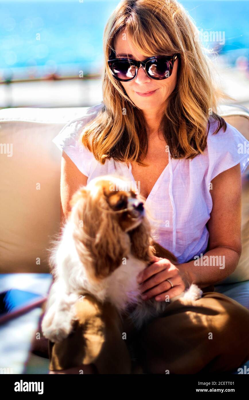 Foto di donna di mezza età godendo di una giornata di sole mentre si rilassa sul mare con il suo cucciolo di cavalier re charles. Foto Stock