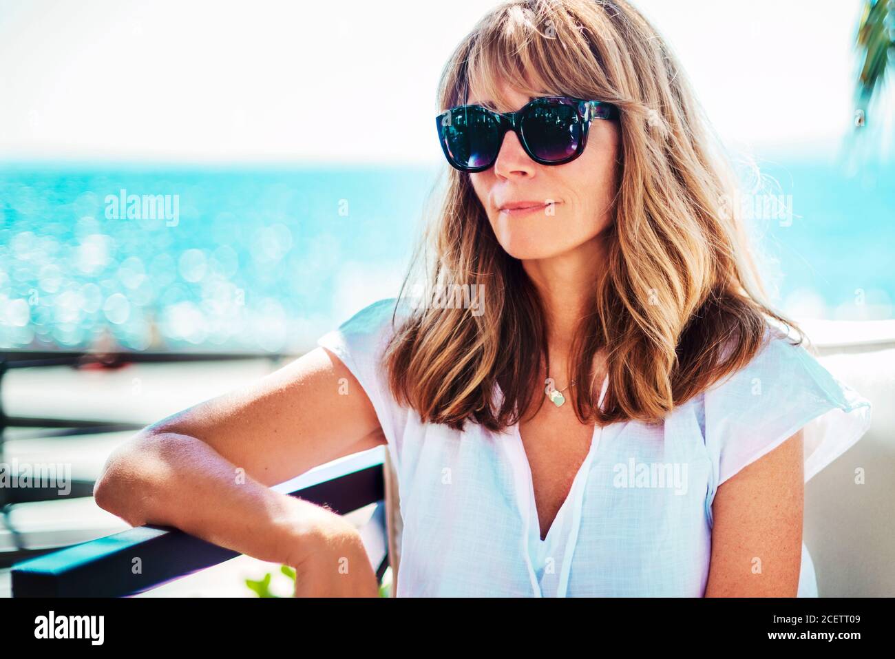 Ritratto di una donna felice che gode del sole estivo mentre si rilassa sul divano lounge vicino al mare. Foto Stock