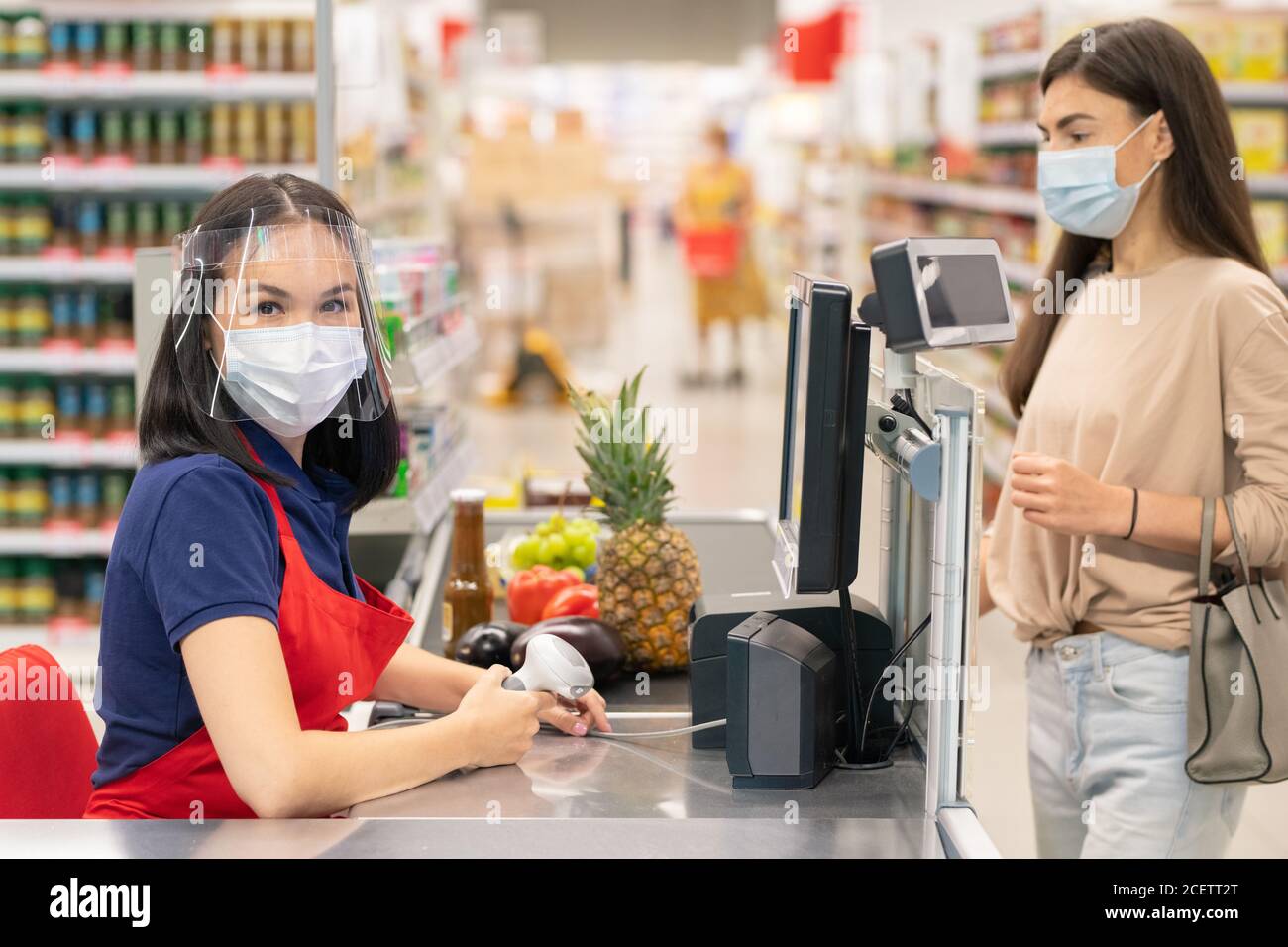 Lavoratore e cliente moderno del negozio seguendo le norme di protezione personale durante i giorni di quarantena Covid-19, indossando maschere Foto Stock