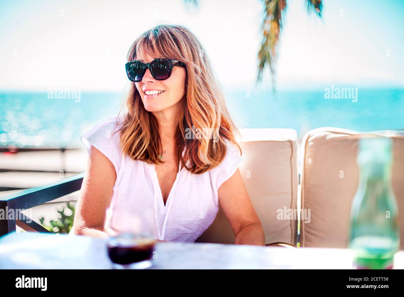 Ritratto di una donna felice che gode del sole estivo mentre si rilassa sul divano lounge vicino al mare. Foto Stock