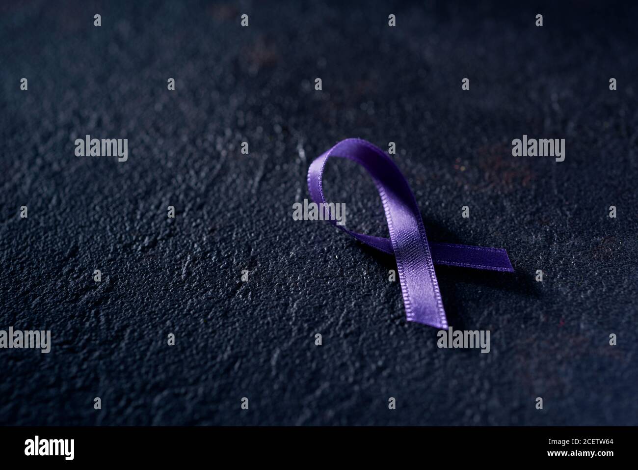 Un nastro di consapevolezza viola, per la consapevolezza della malattia di Alzheimers, su una superficie nera testurizzata Foto Stock