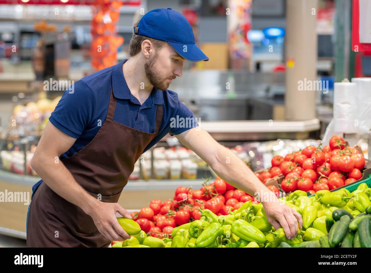 Moderno operaio di supermercato che indossa uniforme che stabilisce verdure fresche, tiro orizzontale medio, spazio di copia Foto Stock