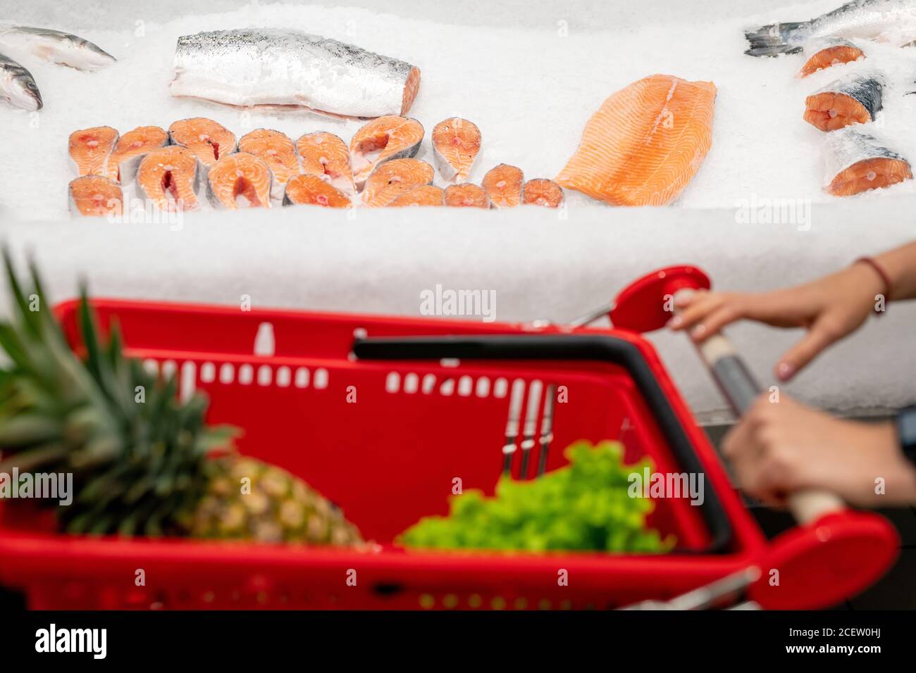 Donna irriconoscibile con carrello di acquisto scegliendo pesce di salmone fresco in negozio moderno, spazio di copia Foto Stock