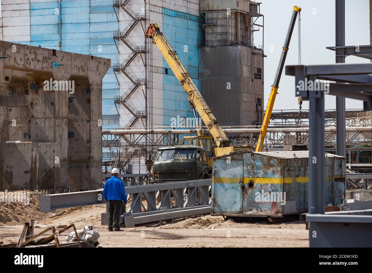 Ristrutturazione dell'impianto obsoleta. Sviluppo di un nuovo edificio industriale. Antico edificio blu, gru mobili, condotte, costruzioni in metallo e calcestruzzo, lavoratore. Foto Stock