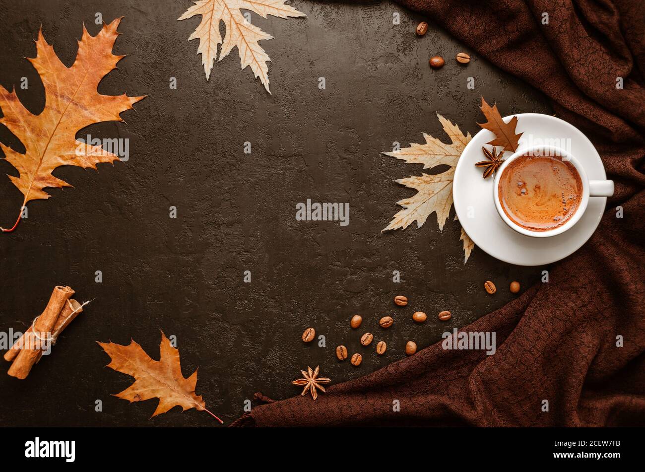 Autunno piatto posato. Tazza di caffè, sciarpa di pashmina marrone, foglie d'autunno, bastoncini di cannella e chicchi di caffè su sfondo nero. Spazio di copia. Vista dall'alto Foto Stock