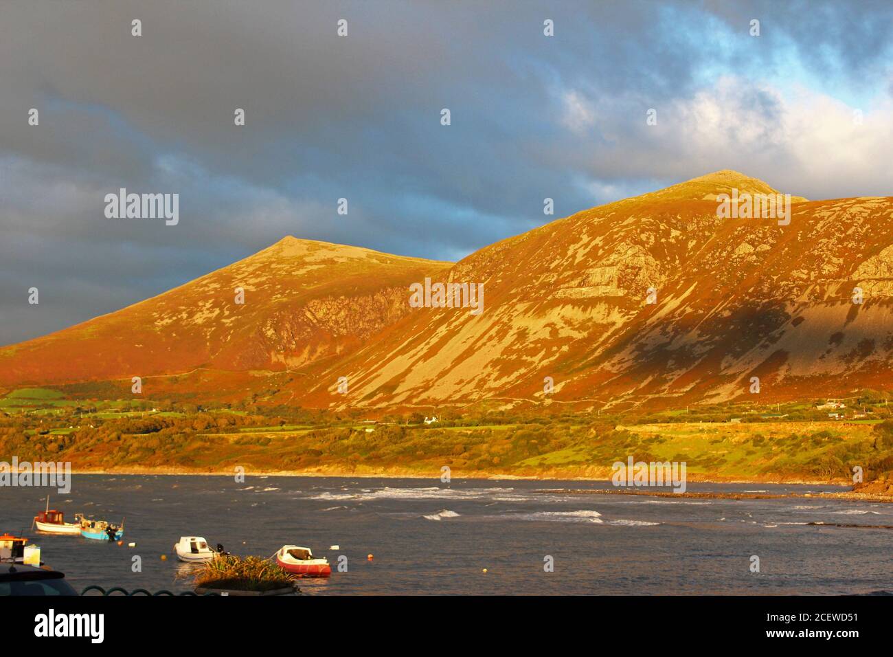 Bella luce tramonto sulle montagne (Yr Eifl) con il mare di fronte a loro e le nuvole scure a Trefor, Galles del Nord Foto Stock