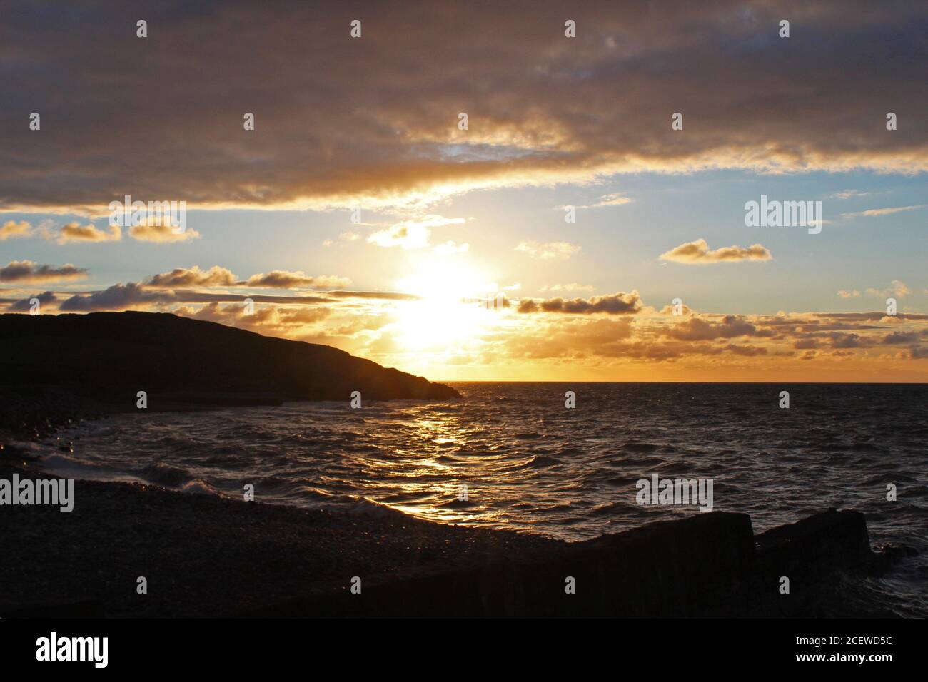 Splendido tramonto dorato e nuvoloso su una baia di mare e promontorio a Trefor, Galles del Nord Foto Stock