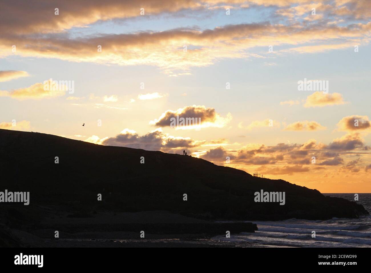Splendido tramonto dorato e brillante su un promontorio e una baia di mare con sagome di gente a Trefor, Galles del Nord Foto Stock