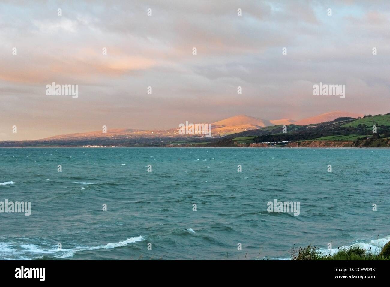 Montagne illuminate al tramonto e città in lontananza sul Mare d'Irlanda a Trefor, Galles del Nord Foto Stock