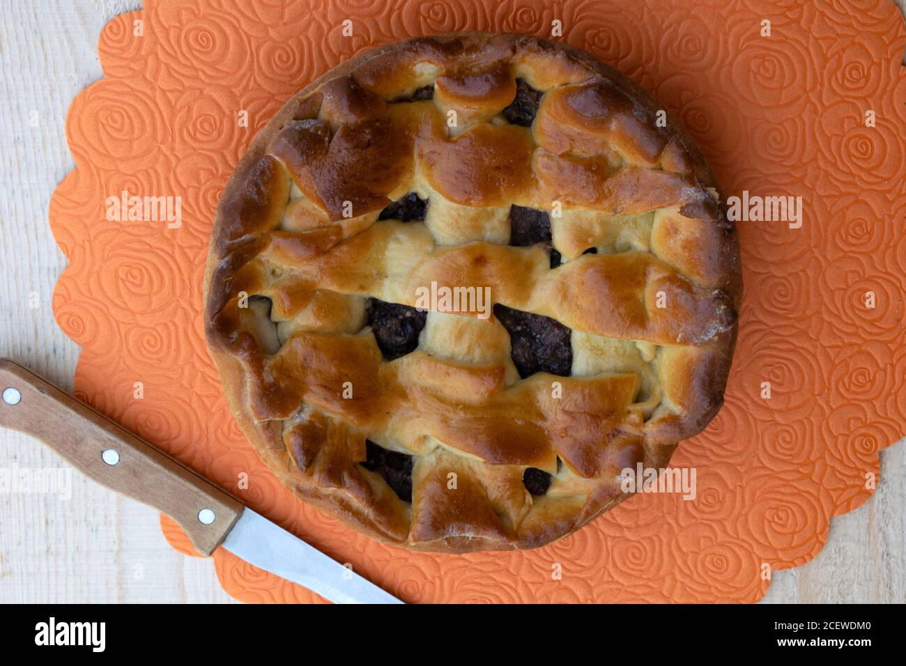 cucina casalinga, torta di marmellata di mele piena di ciliegia e noci e un coltello si trovano su un tavolo di legno, vista dall'alto Foto Stock