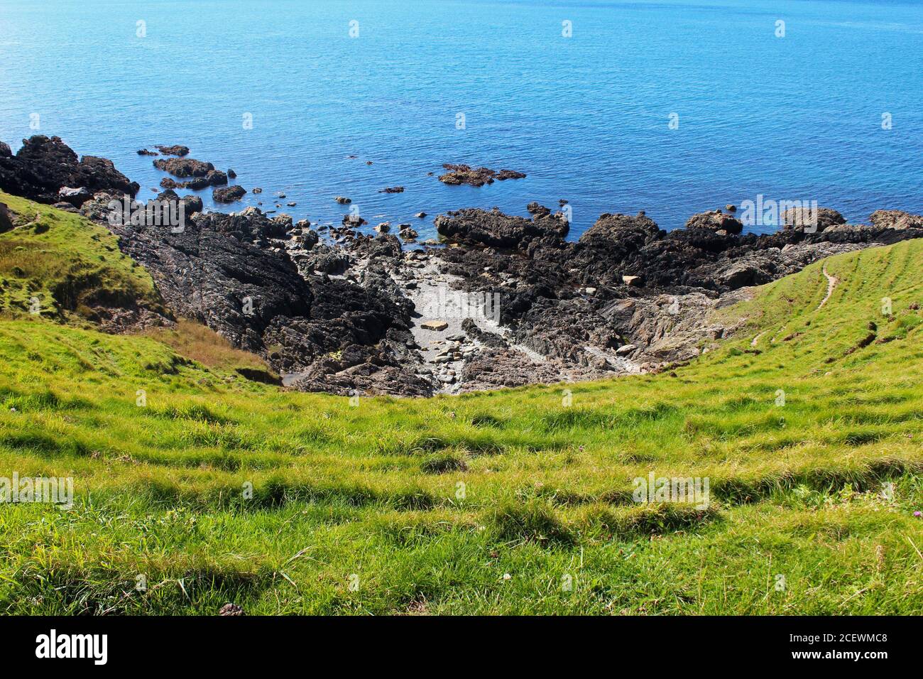 Un affioramento roccioso in fondo ad una collina di erba vicino al blu Mare d'Irlanda in una giornata di sole sulla costa di Porth Colmen, Galles del Nord Foto Stock