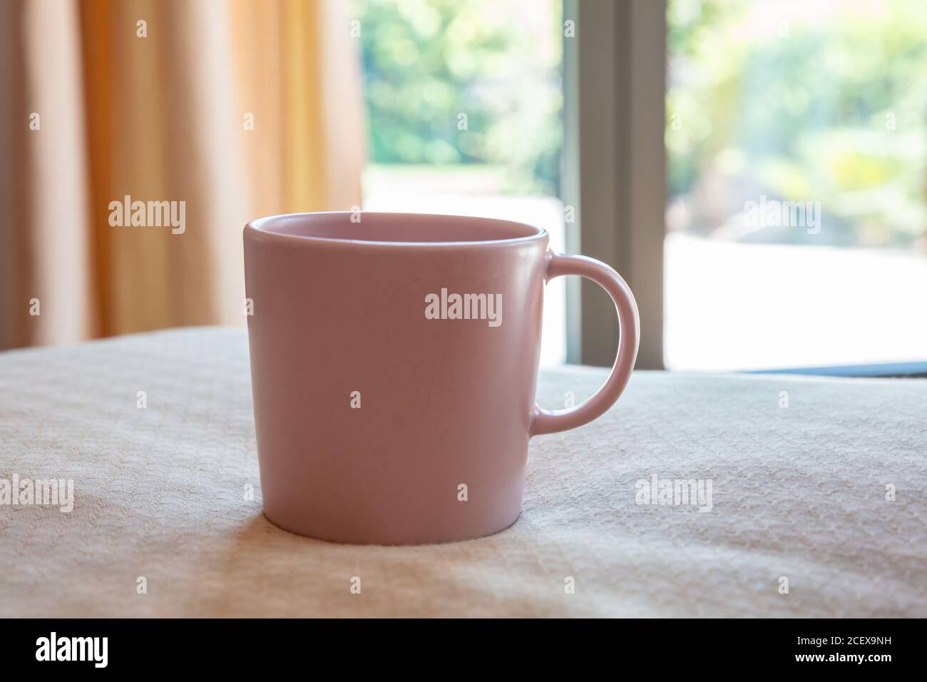 Tazza di caffè sul letto, sullo sfondo della camera da letto. Mockup di bevande calde. Tazza vuota di colore rosa con maniglia pubblicizza, modello di branding Foto Stock