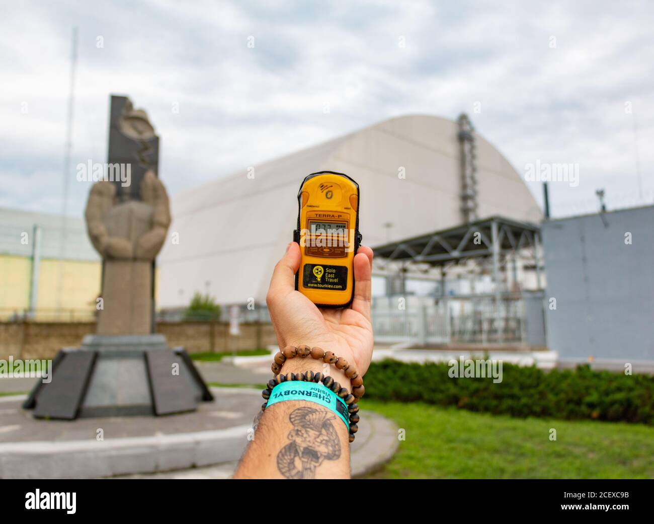 Una foto di una persona in possesso di un contatore giger nella parte anteriore della centrale nucleare di Cernobyl. Foto Stock