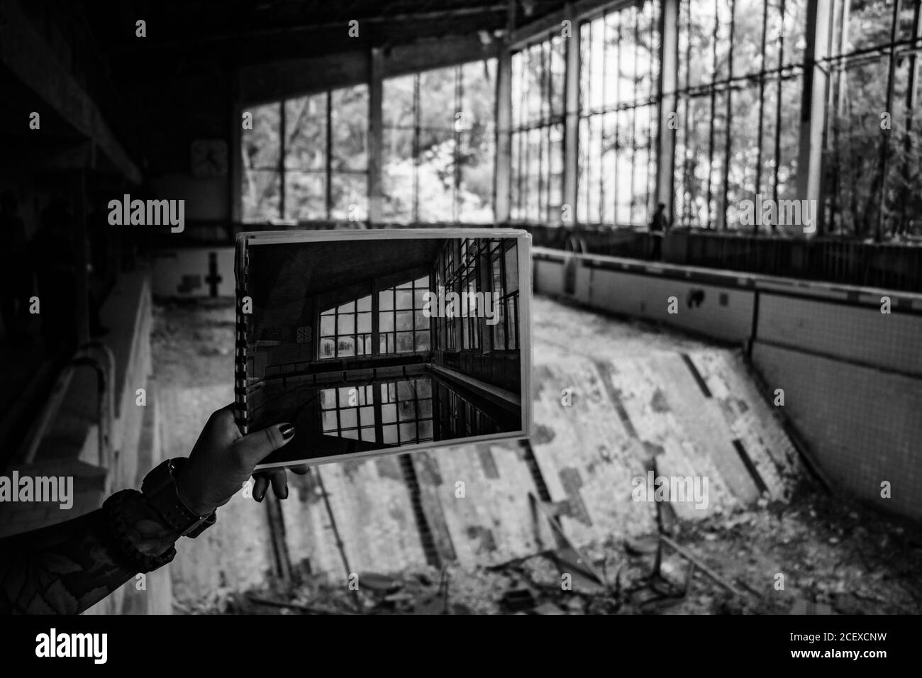 Una foto in bianco e nero di qualcuno che mostra una foto della piscina di pripjat contro l'attuale scenario abbandonati. Foto Stock
