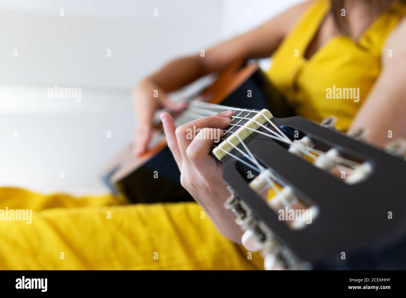 Vista laterale di una donna di talento ritagliata e irriconoscibile seduta sul letto suonare la chitarra Foto Stock