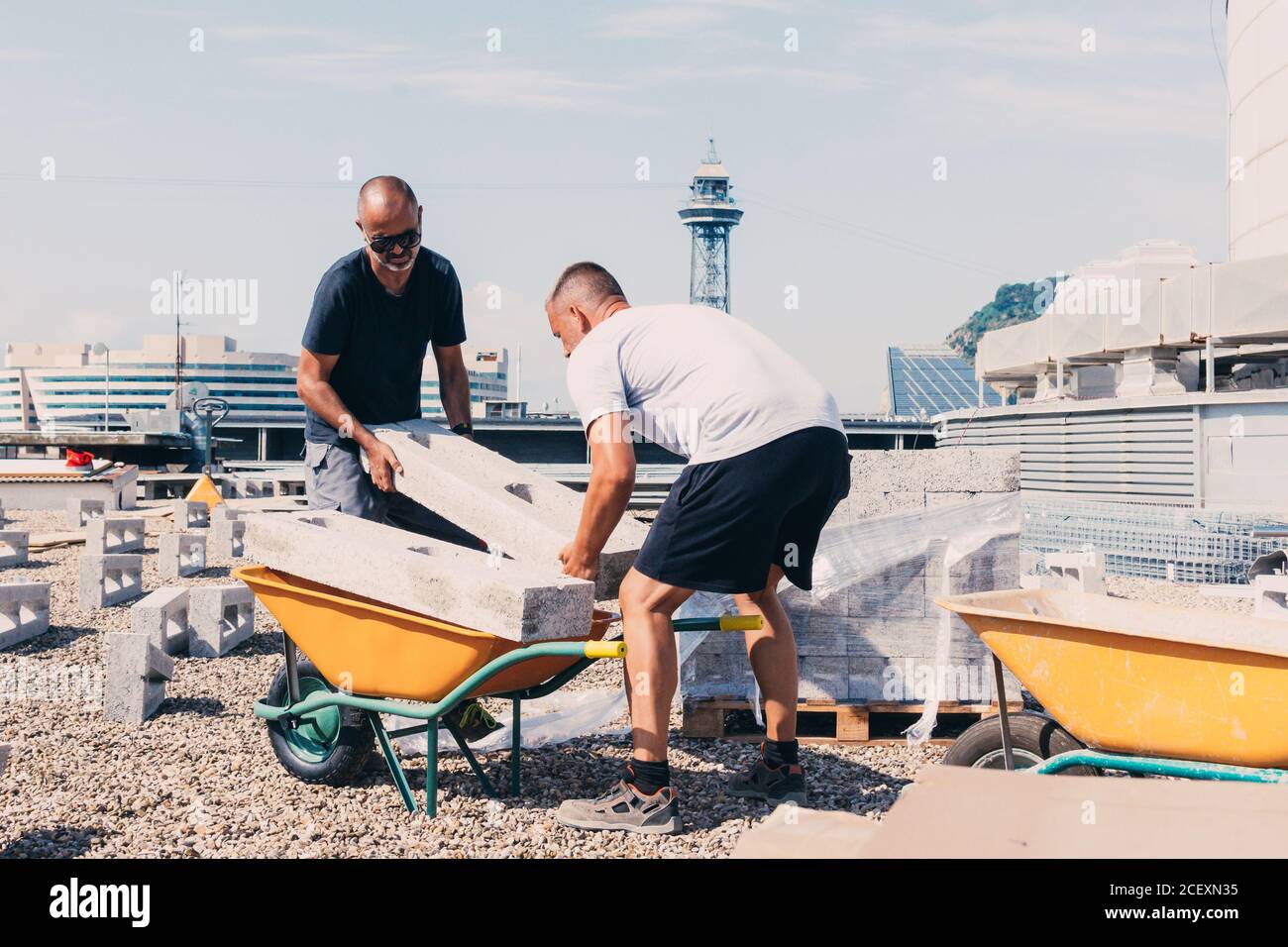 Impiegati di sesso maschile impegnati che trasportano blocchi pesanti di calcestruzzo mentre lavorano dentro cantiere di fabbrica moderna in giornata di sole Foto Stock