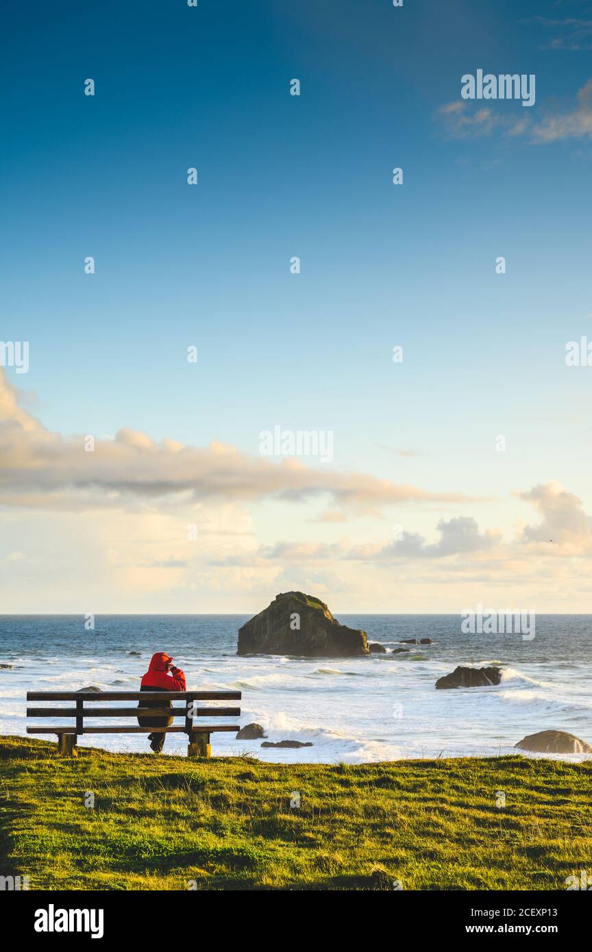 Una persona si siede sulla panchina dall'oceano, praticando la distanza sociale, foto verticale. Foto Stock