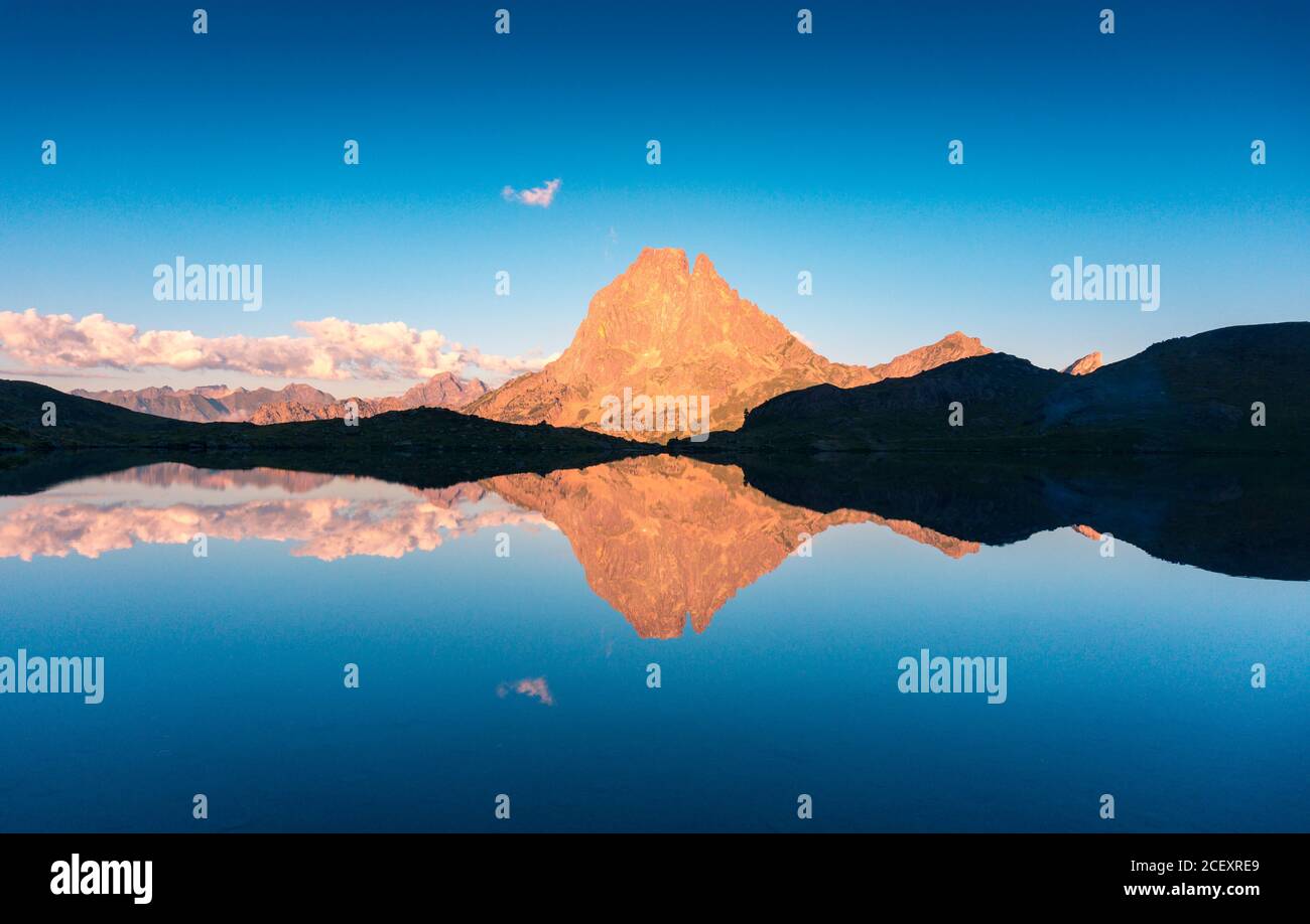 Maestoso scenario di acque calme del lago sullo sfondo di cima di montagna illuminata dalla luce solare sotto il cielo blu Foto Stock