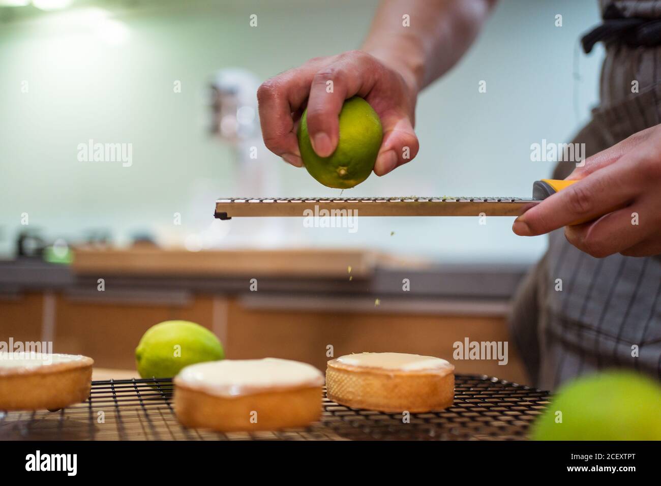 Crop persona in grembiule facendo crostate con cagliata e calce zest che lavora al tavolo da cucina Foto Stock