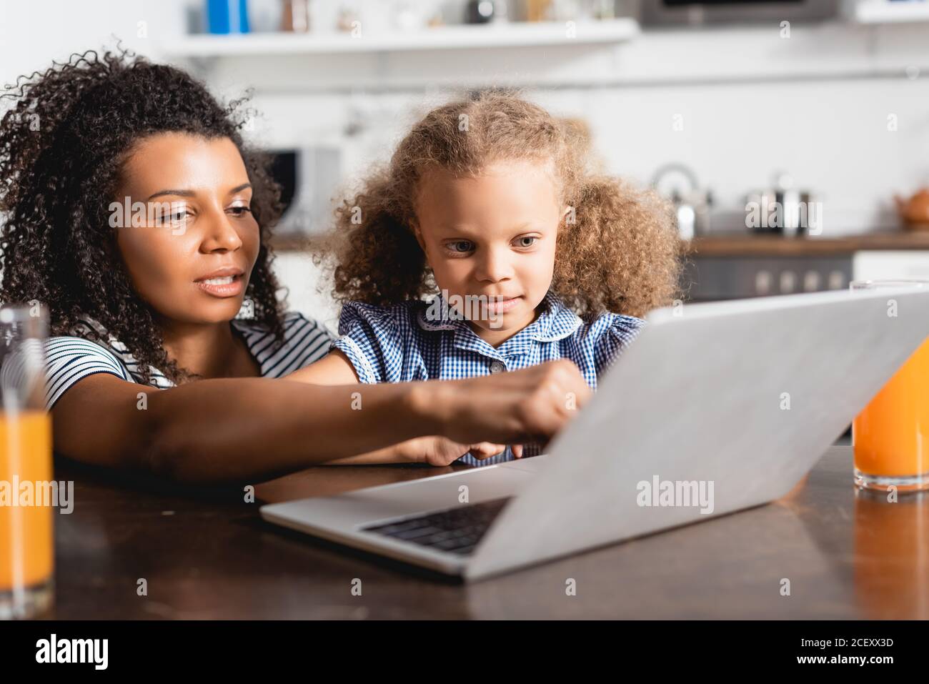 fuoco selettivo della donna afroamericana che punta al laptop vicino figlia concentrata Foto Stock