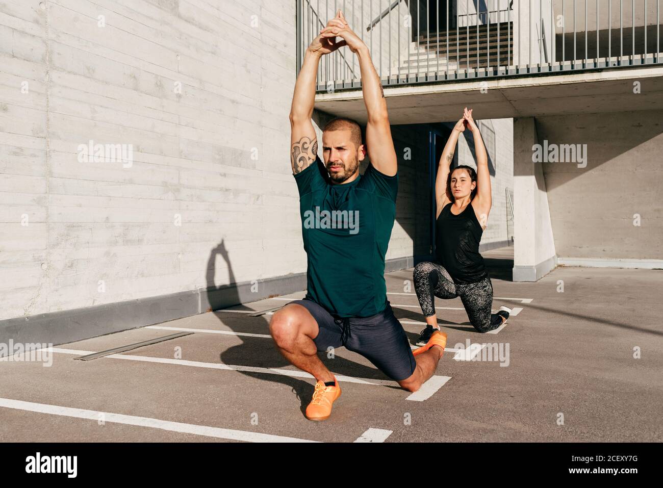 Coppia in abbigliamento sportivo che pratica yoga in Crescent Lunge posa con braccia sollevate e meditating Foto Stock