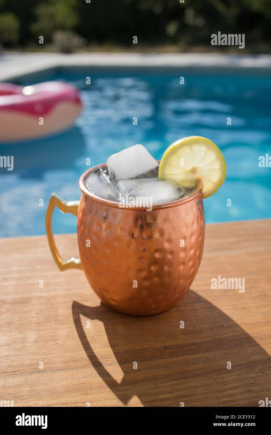 Tradizionale cocktail alcolico muto di Mosca con cubetti di ghiaccio e lime servita in una tazza di rame posta vicino alla piscina Foto Stock