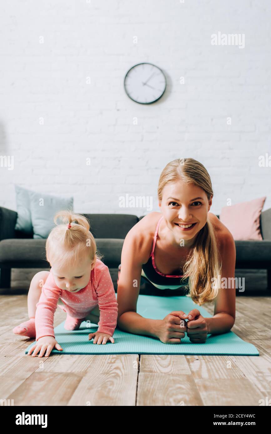 Fuoco selettivo di sportswoman che fa la tavola vicino alla ragazza del bambino sopra tappetino fitness Foto Stock