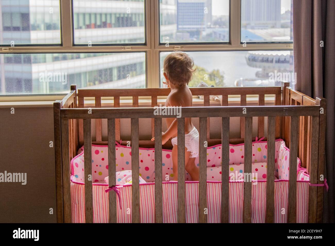 concetto di quarantena. bambino toddler è in piedi nella culla e guardando fuori la finestra al paesaggio urbano dei grattacieli. Foto Stock