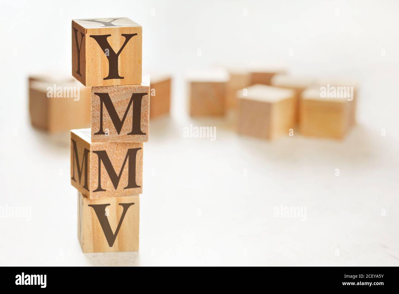 Quattro cubi di legno disposti in pila con lettere YMMV (il che significa che il chilometraggio può variare) su di essi, spazio per testo / immagine in basso a destra angolo Foto Stock